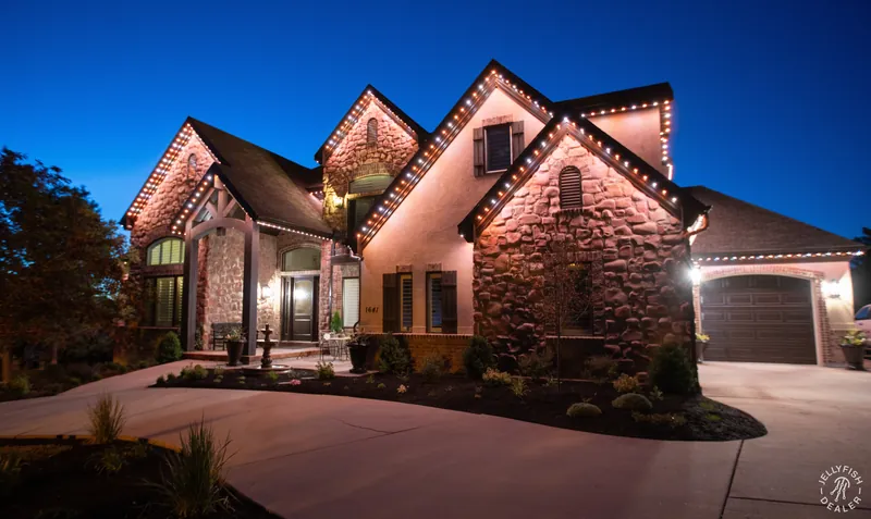 Warm-white permanent roofline lighting on a stone home at dusk